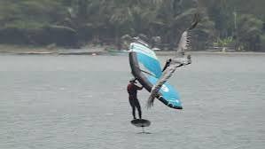 Wing foiler volando bajo sobre el agua con palmeras de fondo en Puerto Velero