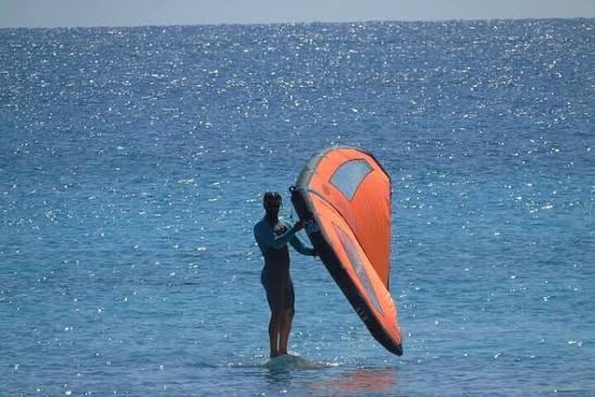 Practicante de wing foil sosteniendo el ala naranja antes de navegar en Puerto Velero